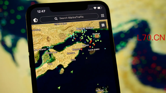 2026 年 4 月 8 日，法国克雷泰伊，一部智能手机屏幕显示 MarineTraffic 应用程序，背景为卫星视图，画面中霍尔木兹海峡附近密布大量船舶信标。当时美国与伊朗刚达成外交协议，重新开放这条战略水道供国际航运通行。